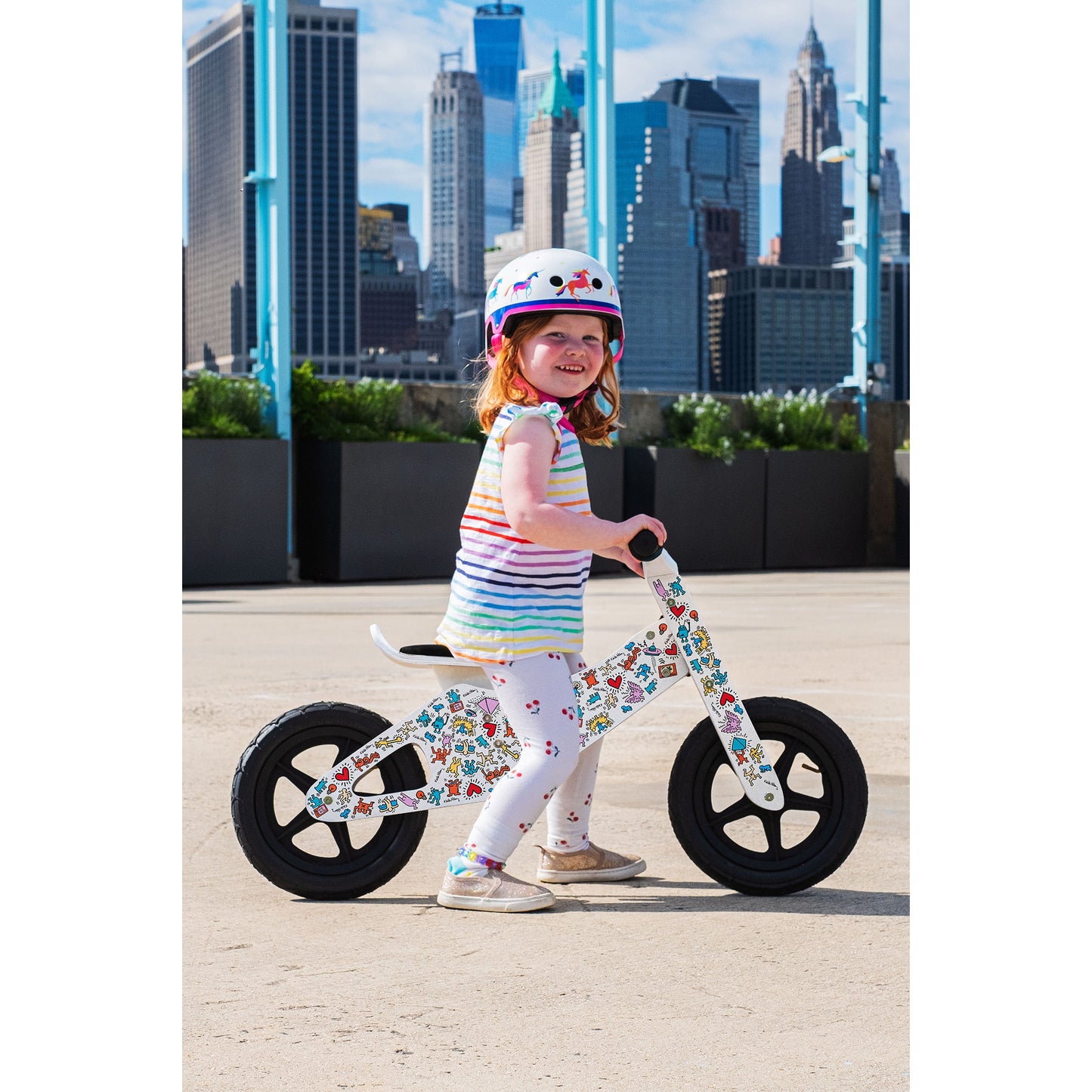 Child on a Keith Haring limited edition balance bike with a cityscape in the background