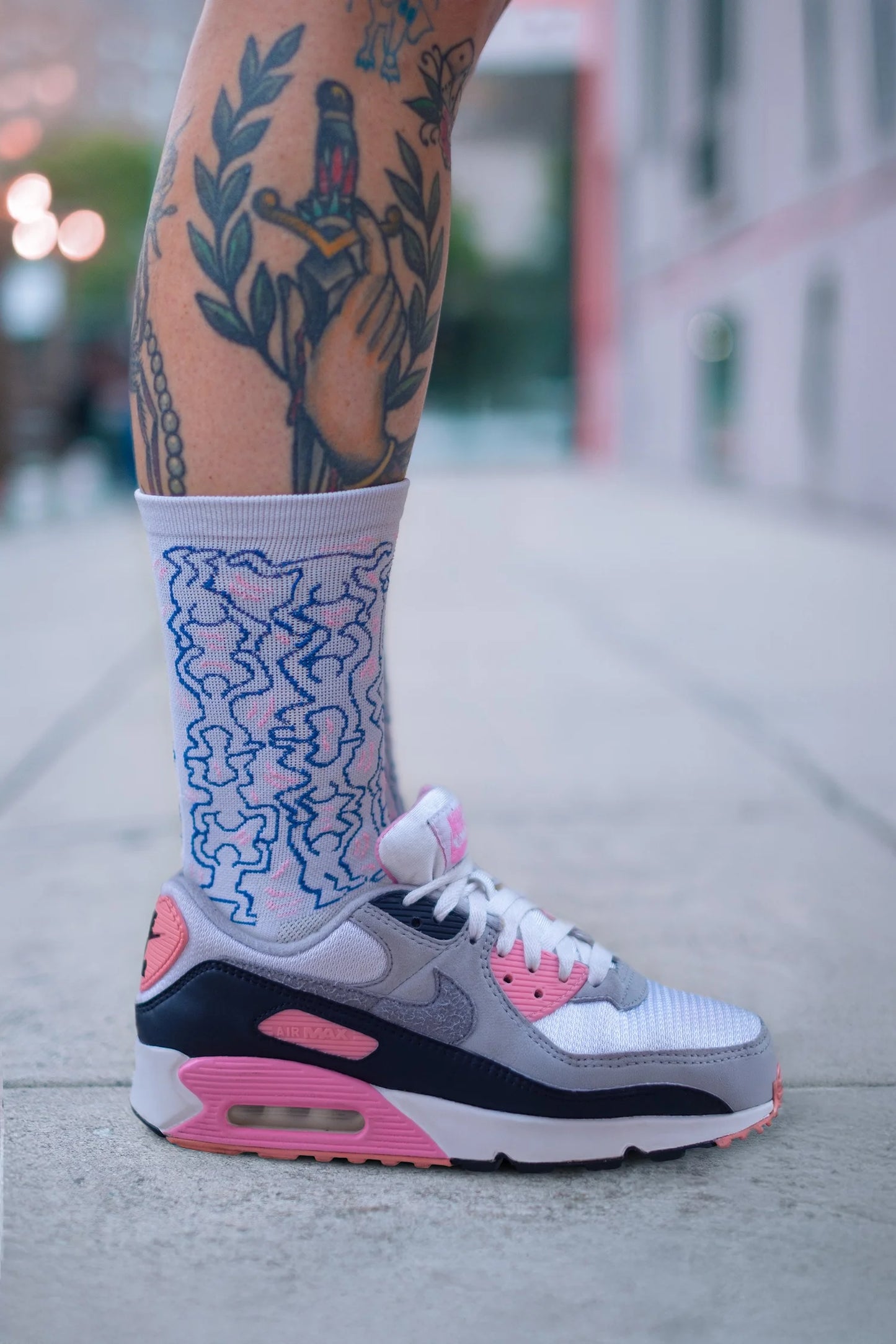 Cyclist wearing Affinity x Keith Haring “Dancing Figures” white and pink cycling socks with Haring’s iconic outlined characters, paired with pink Nike Air Max shoes.