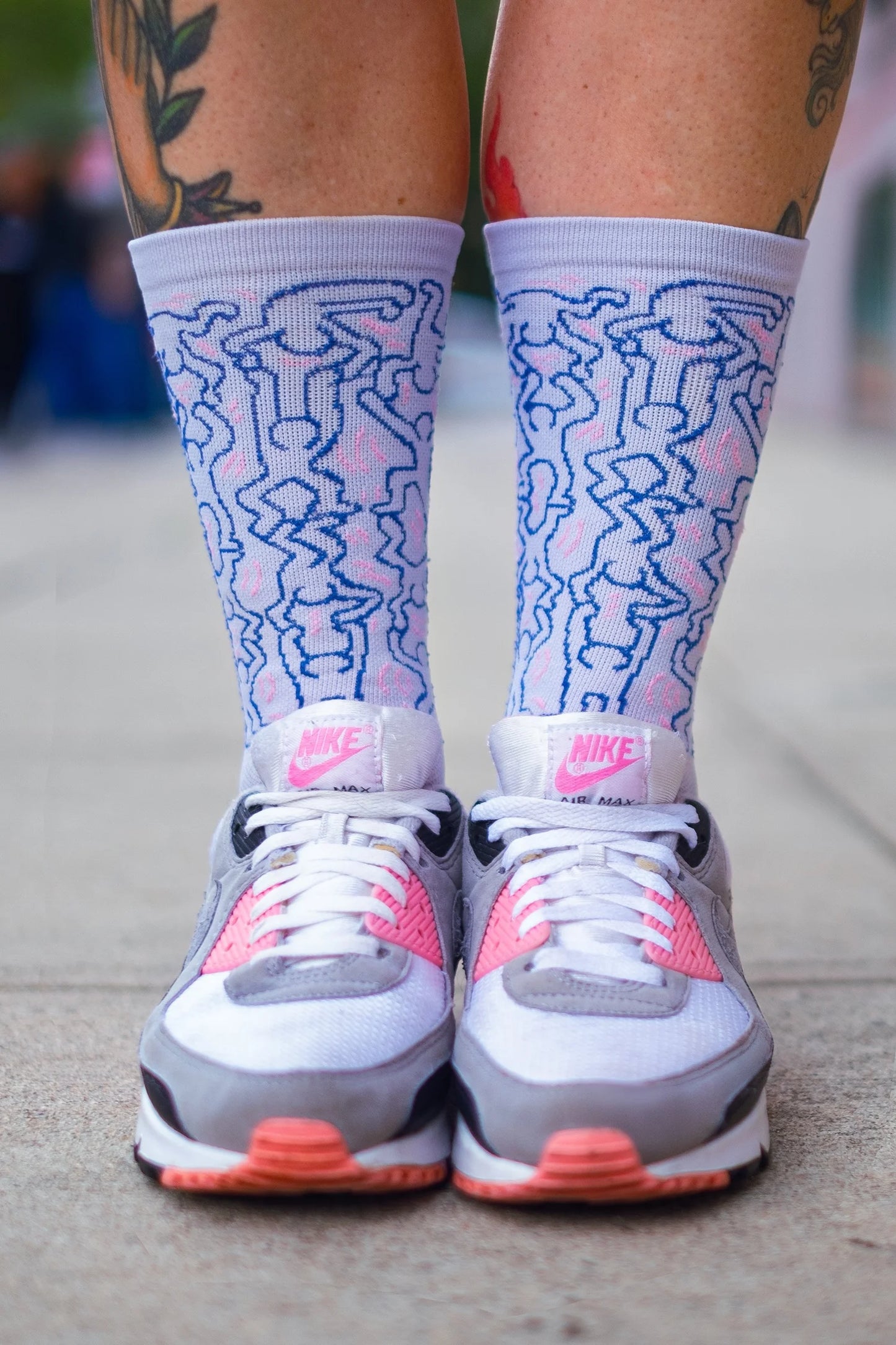 Cyclist wearing Affinity x Keith Haring “Dancing Figures” white and pink cycling socks with Haring’s iconic outlined characters, paired with pink Nike Air Max shoes.