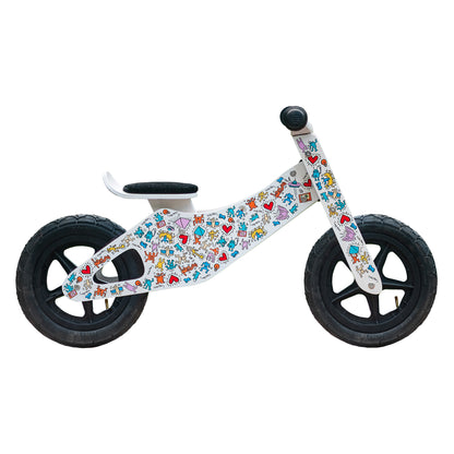 Children's balance bike with colorful Keith Haring graphics in front of a white background