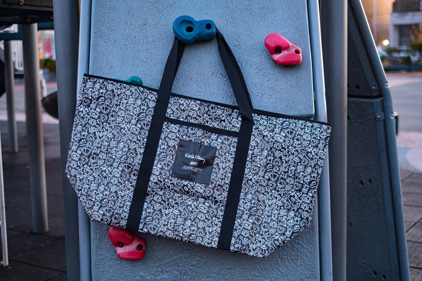 Keith Haring x Affinity XXL Tote Bag hanging from a jungle gym.