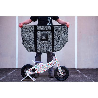 Person holding a Keith Haring x Affinity XXL Tote Bag with a small balance bike on the ground.