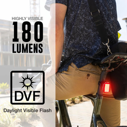Person riding a bicycle with an illuminated  Nite rider VMAX +180 bike taillight, highlighting '180 Lumens' and 'DVF' (Daylight Visible flash)