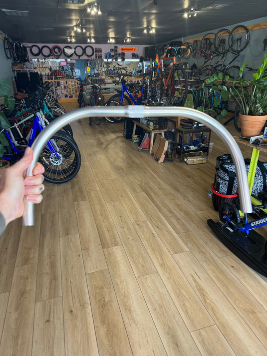 Hand holding Nitto B617 Promenade handlebar inside Taylor Bike Co. shop – polished silver finish, swept-back shape.