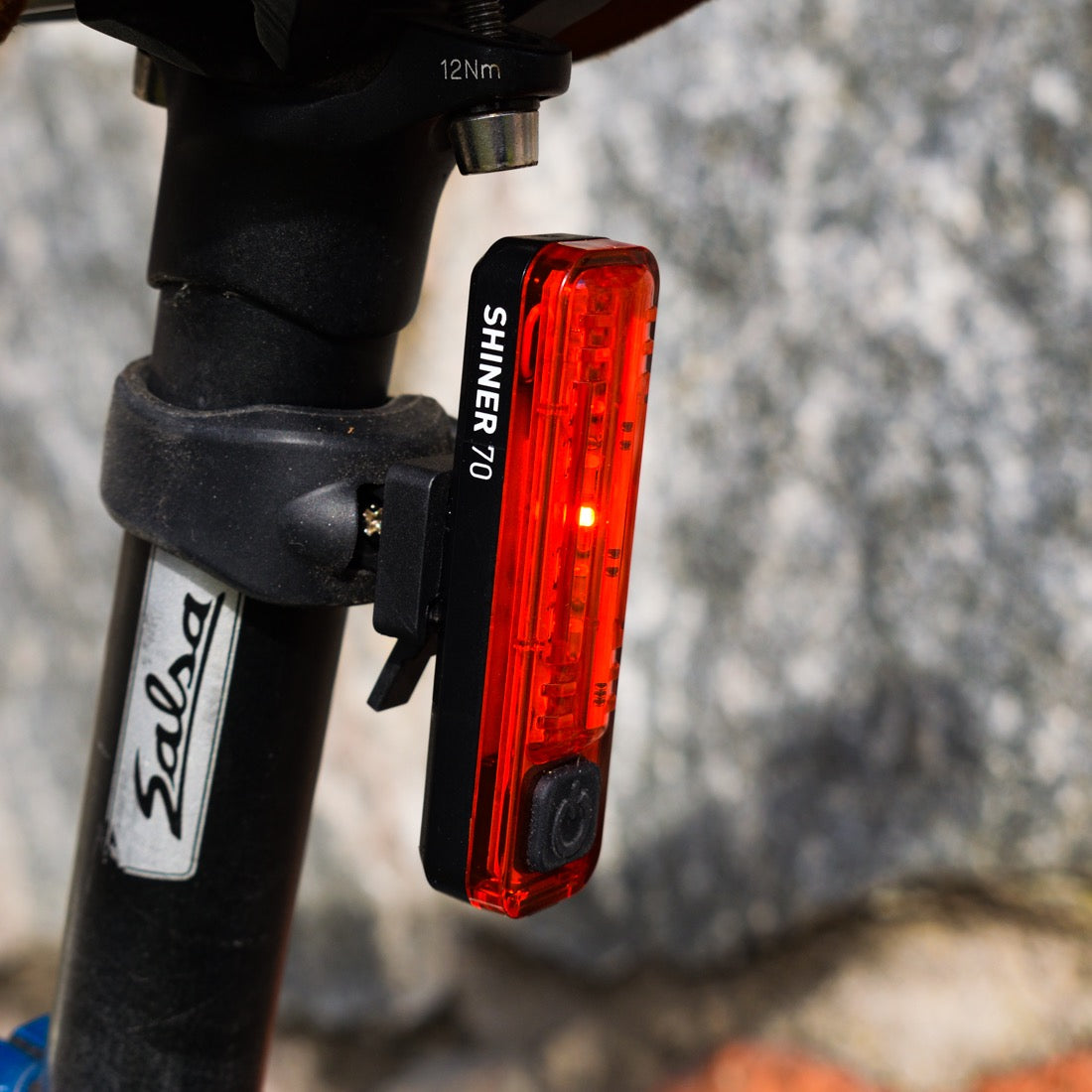 Red bike taillight attached to a bicycle seat post with a blurred natural background.