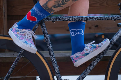 Close-up of Affinity x Keith Haring “Bike Heart” royal blue cycling socks with red heart and bike graphic, worn with floral sneakers.