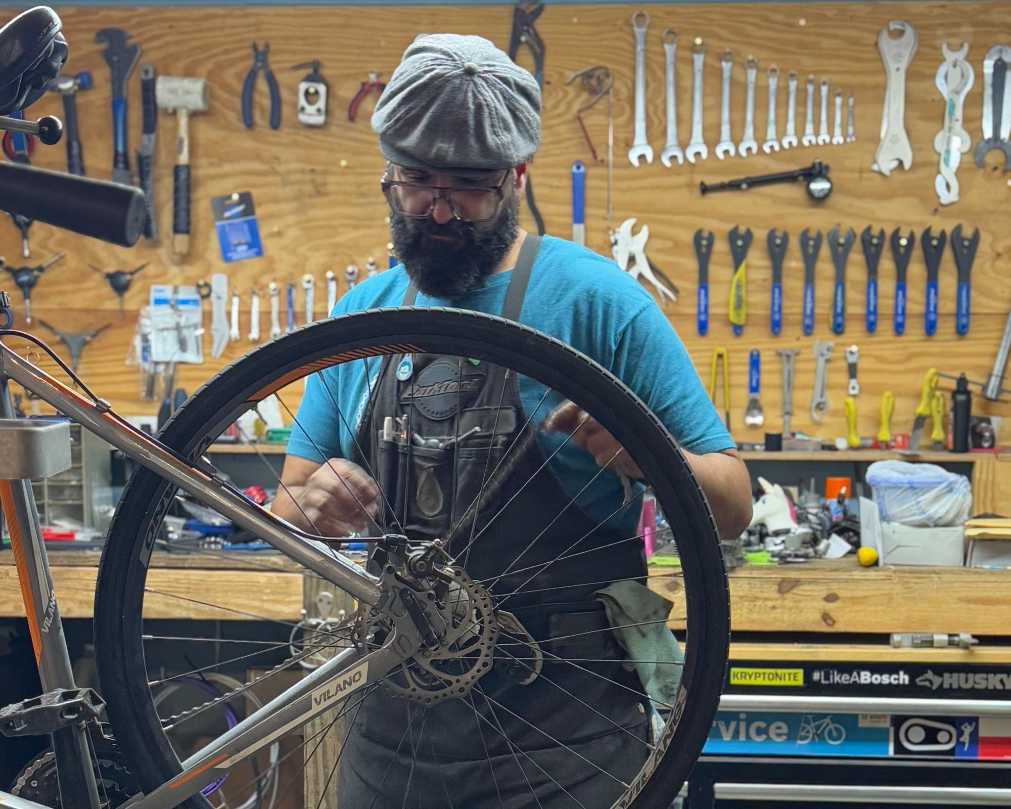 Person working on a bicycle wheel in a workshop with tools and equipment in the background.